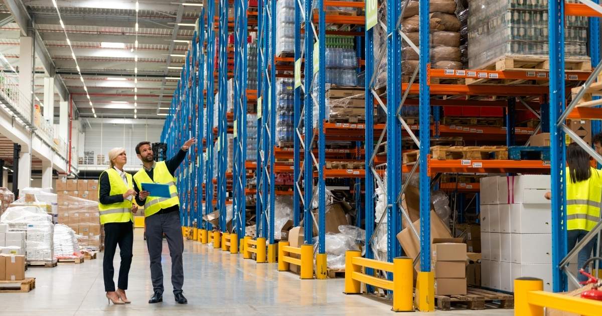 Warehouse workers in hi-vis reviewing stock on industrial shelving