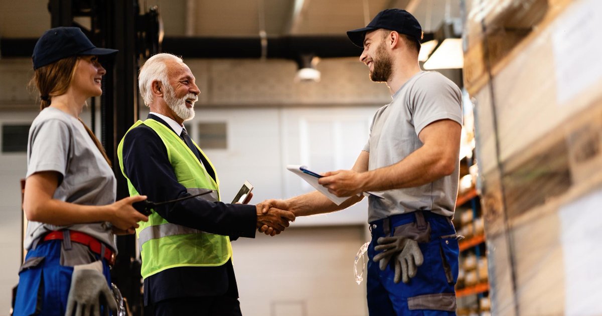 Industrial supplier manager in high-vis vest shaking hands with a warehouse worker holding a clipboard while a female colleague looks on in an Australian warehouse showing a trusted supplier partnership