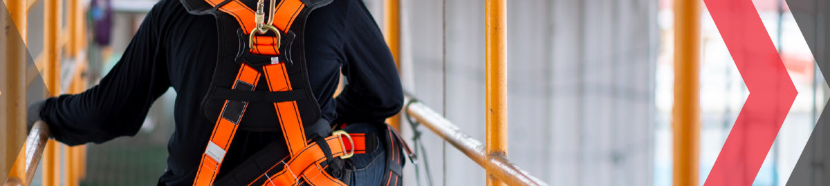 Worker wearing an orange full-body safety harness on scaffolding at a construction site.