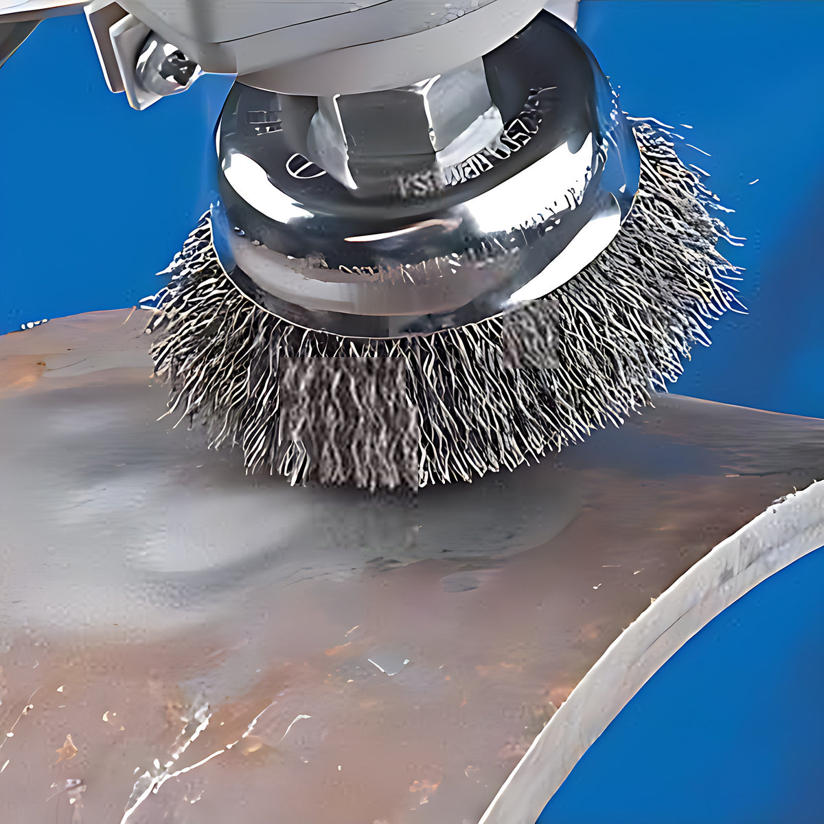 Pferd TBU stainless steel crimped cup brush on an angle grinder, cleaning rust from a curved steel pipe, blue background