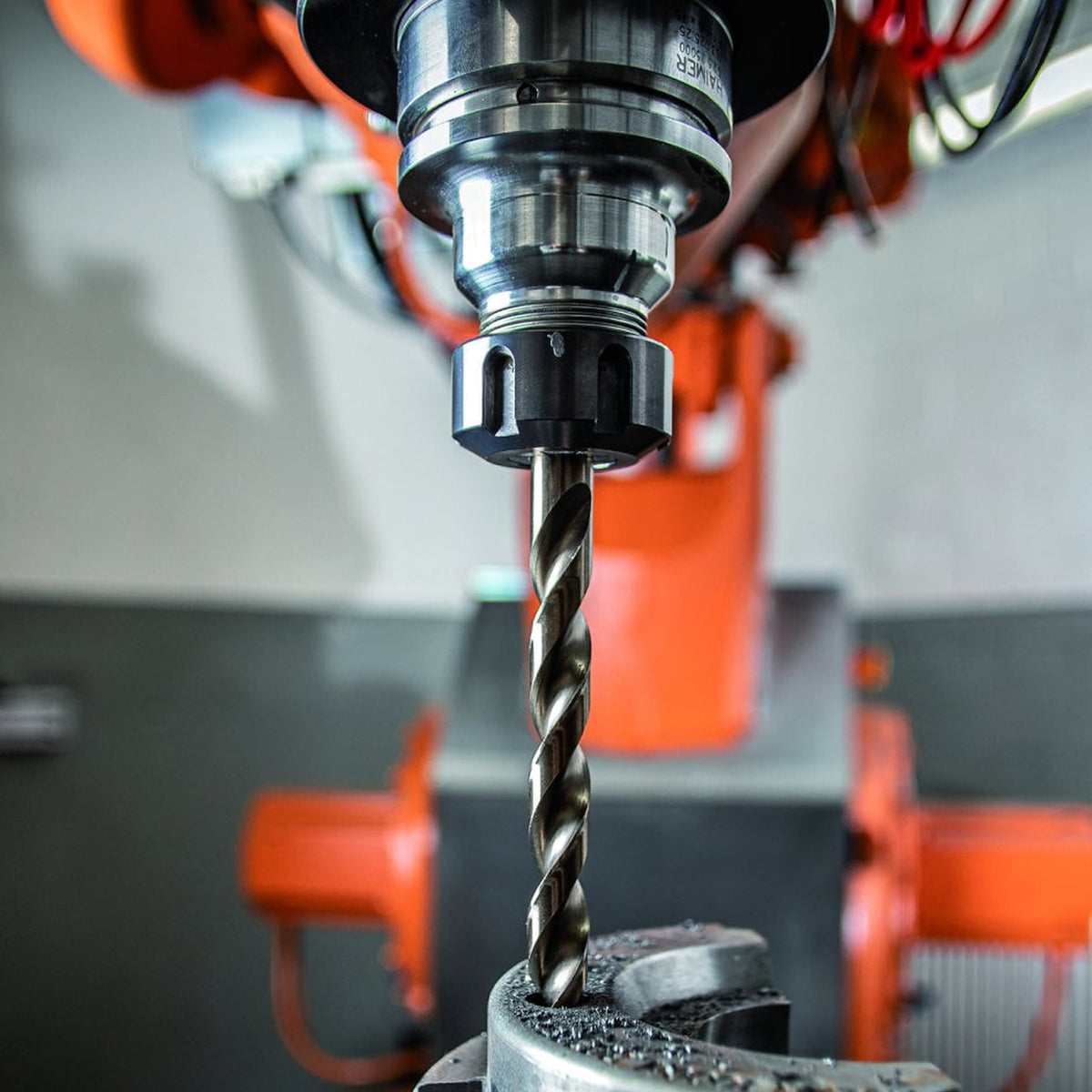 Pferd 8-piece 3 to 8 mm HSSG N Steel twist drill in use, drilling a part clamped in a machine vice, orange machine behind