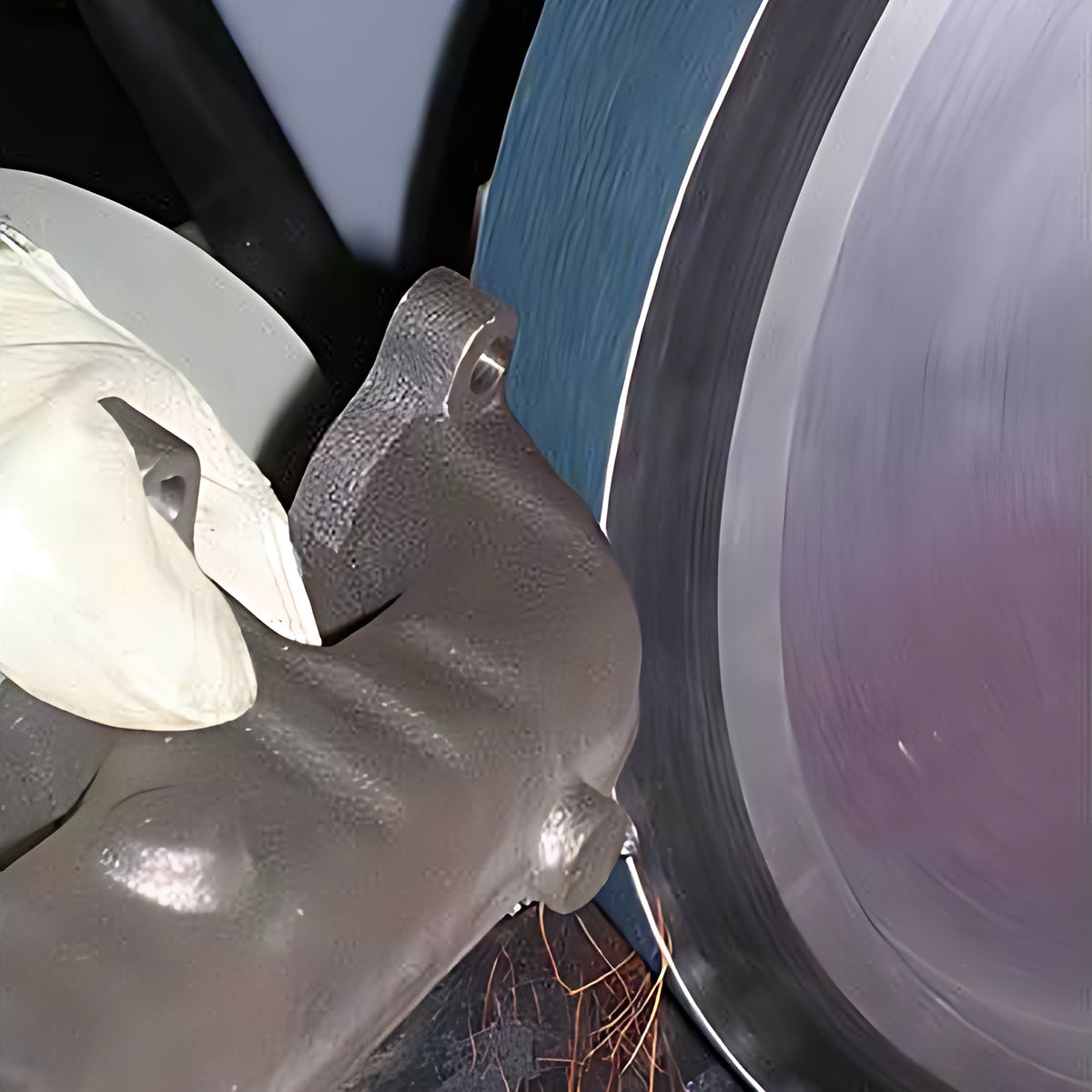 Pferd blue zirconia linishing belt 50 x 1520 mm in use, gloved hand holding a metal casting against the belt on a wheel