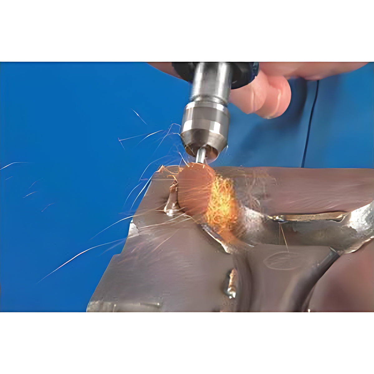 Pferd POLICAP PC ZYA cap, small red-orange abrasive cap on a rotary tool throwing sparks while grinding a metal casting, blue background