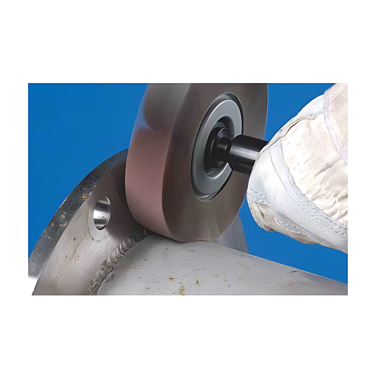 Pferd FR Unmounted Flap Wheel, Aluminium Oxide, 100 x, gloved hand holding a flap wheel on a shaft against the weld at a steel pipe flange, blue background